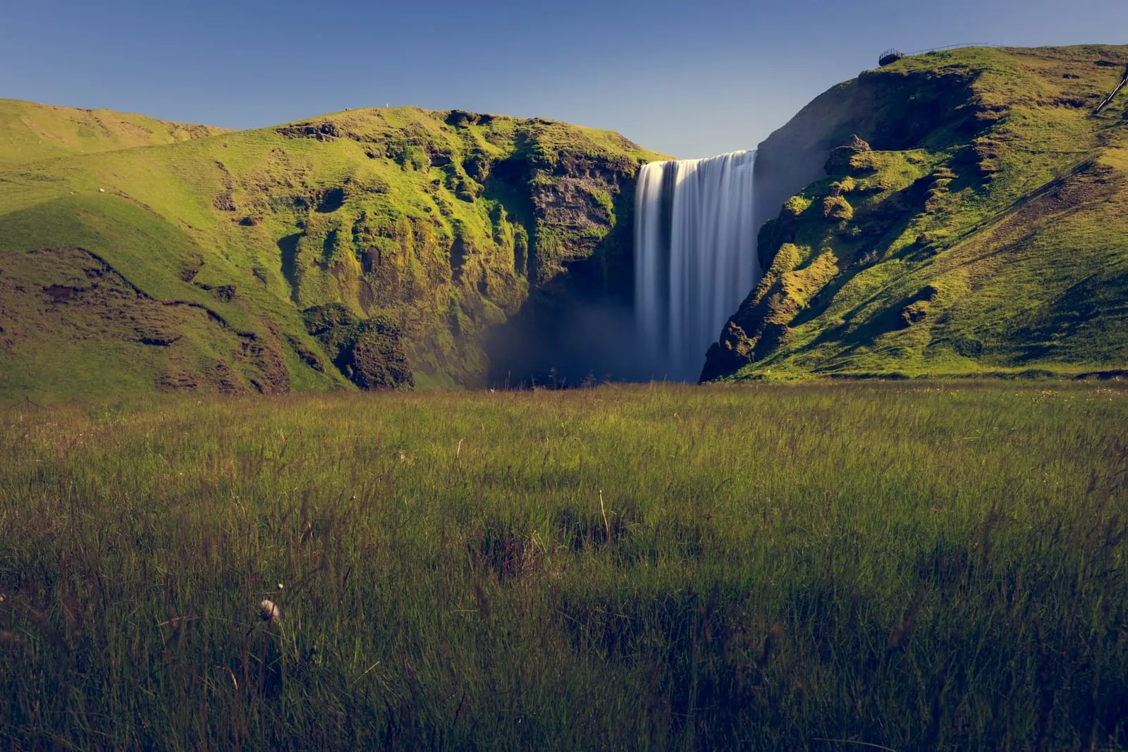 A majestic waterfall cascades down a green hill.