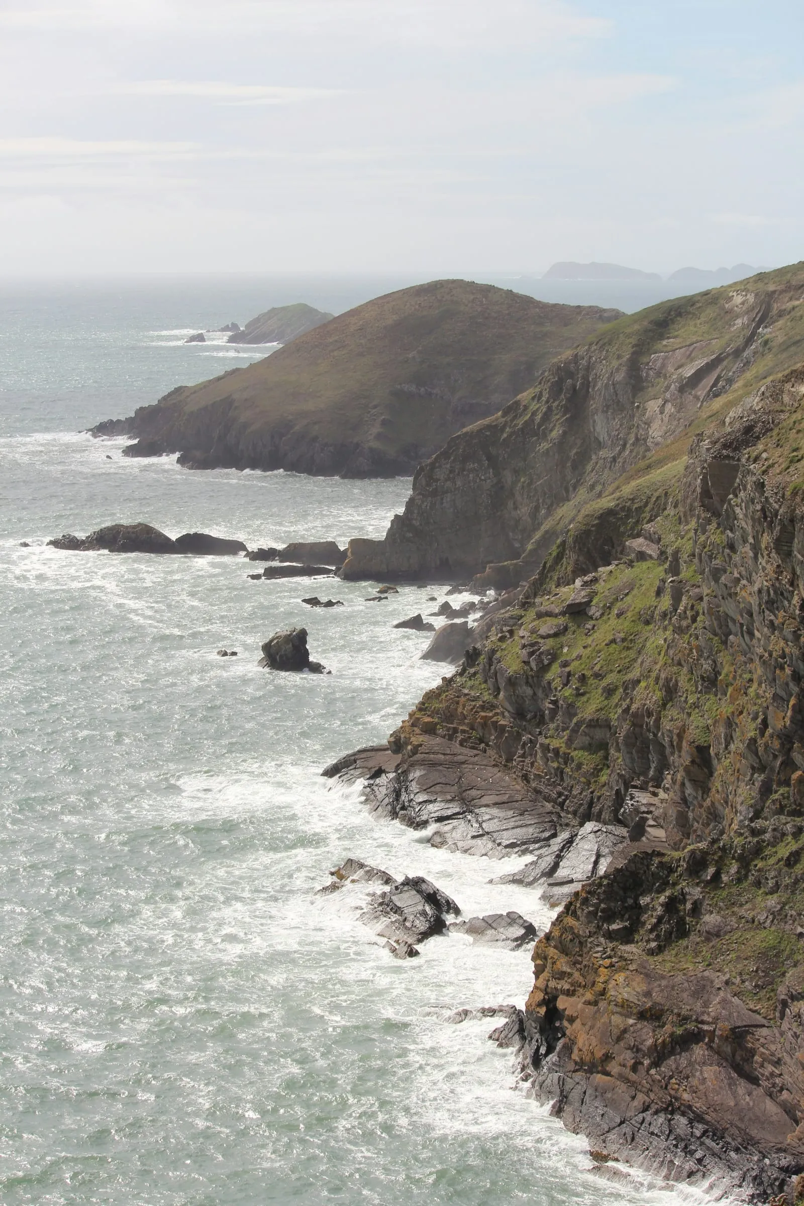 Rugged coastline meets crashing waves under a cloudy sky.